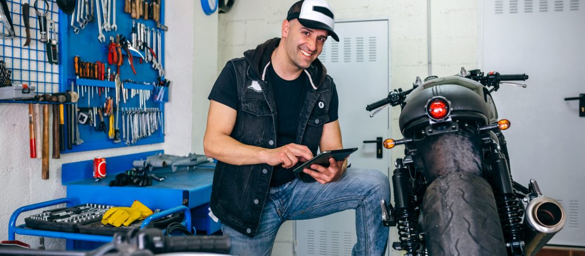 Mechanic posing checking custom motorcycle with tablet in his workshop